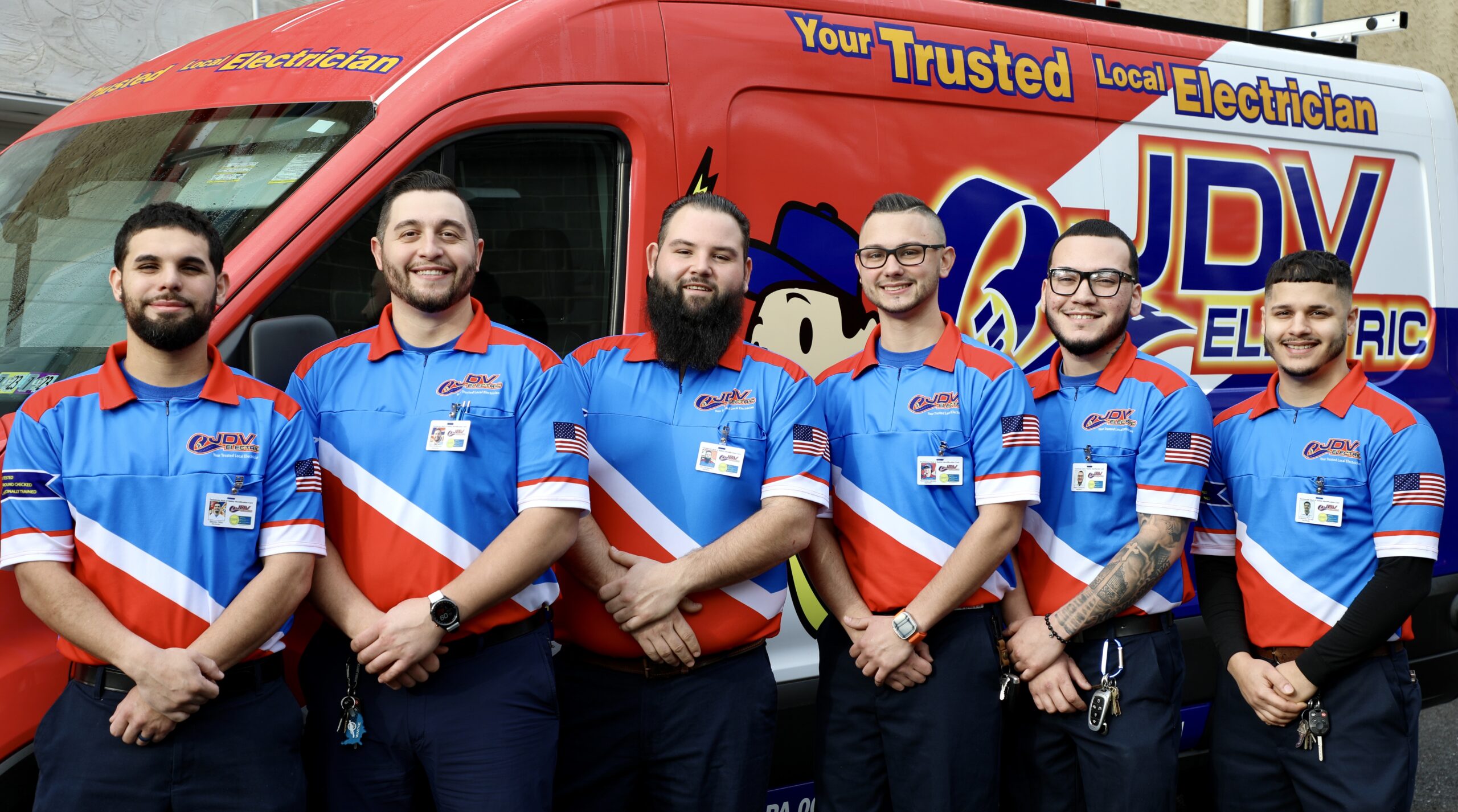 JDV Electric row of electricians in branded polos, standing together in front of a service van.