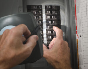 A pair of hands throwing circuit breaker at residential service panel while other hand holds a flashlight