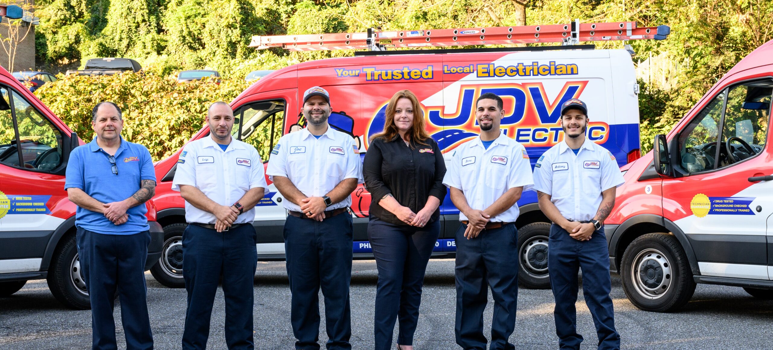 Six JDV staff members standing together in a row outside, with three service vans parked behind them.