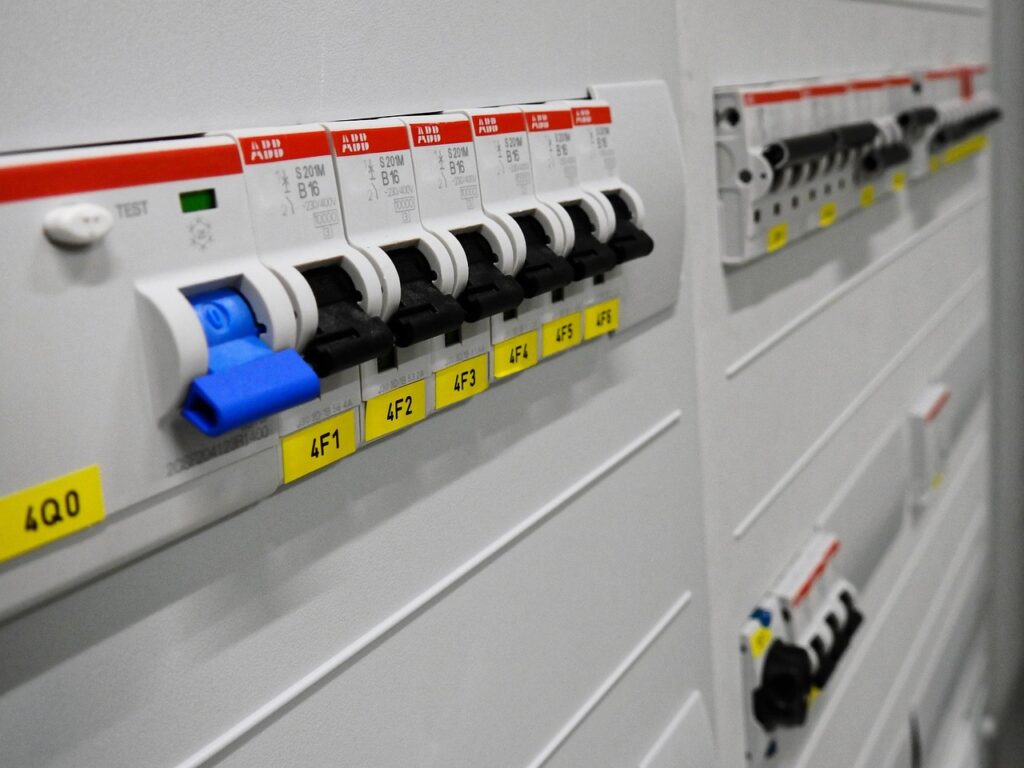 An electrical panel featuring rows of circuit breakers, with one prominent blue switch flipped down and several smaller black switches flipped up, all clearly labeled with yellow tags.